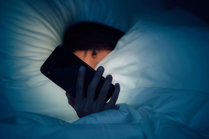 A woman curled up under a blanket, using her smartphone late at night in bed.