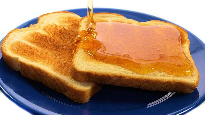 Two slices of toast on a blue plate, with honey being poured over the top slice