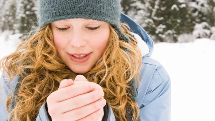 woman warming her hands by blowing on them