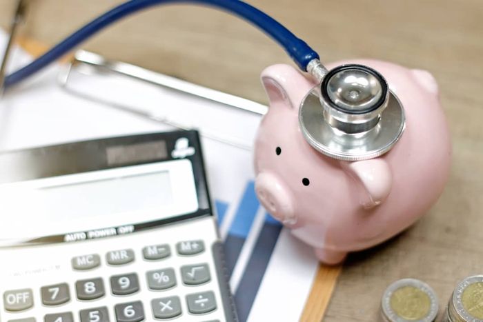 A piggy bank placed beside a calculator and a stethoscope.