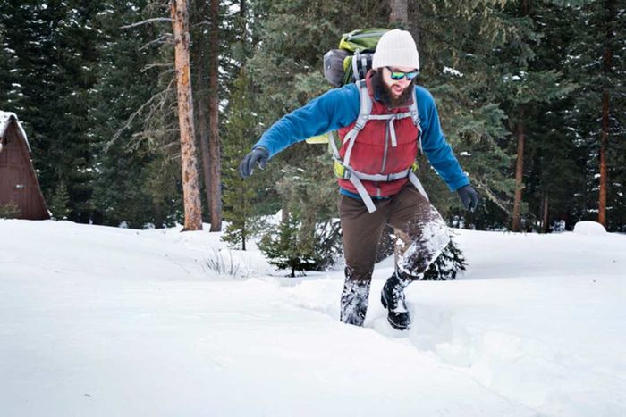A male hiker trudges through deep snow, sinking with each step