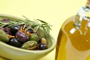 A bottle of olive oil placed beside a bowl of fresh olives