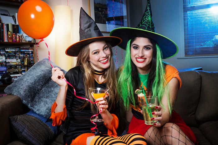 Two women in witch costumes sitting on a sofa.