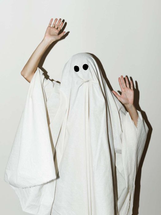 A man in a ghost costume gesturing while standing against a wall