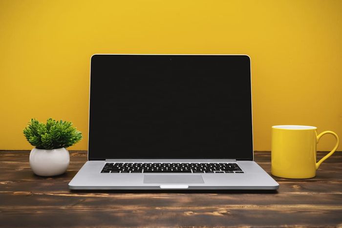 A Laptop and Yellow Coffee Mug on an Office Desk Against a Yellow Background