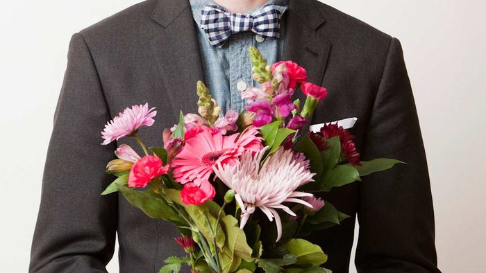 A portrait of a young, handsome man holding a bouquet of flowers.