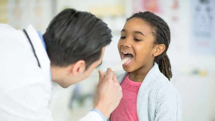A healthcare professional examines a young girl for swollen tonsils.