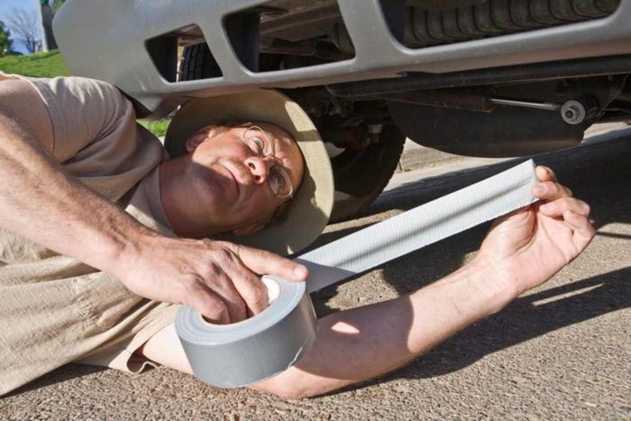 A man using duct tape to repair the underside of a vehicle.