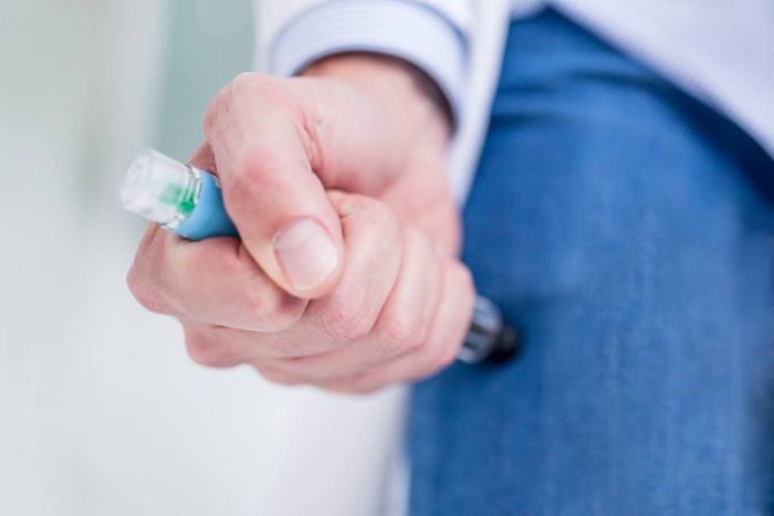 A woman administering an EpiPen injection to herself.