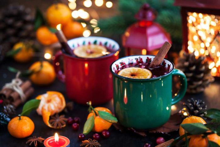 A red and green mug filled with mulled wine, garnished with an orange slice and cinnamon stick, placed on a festive table.