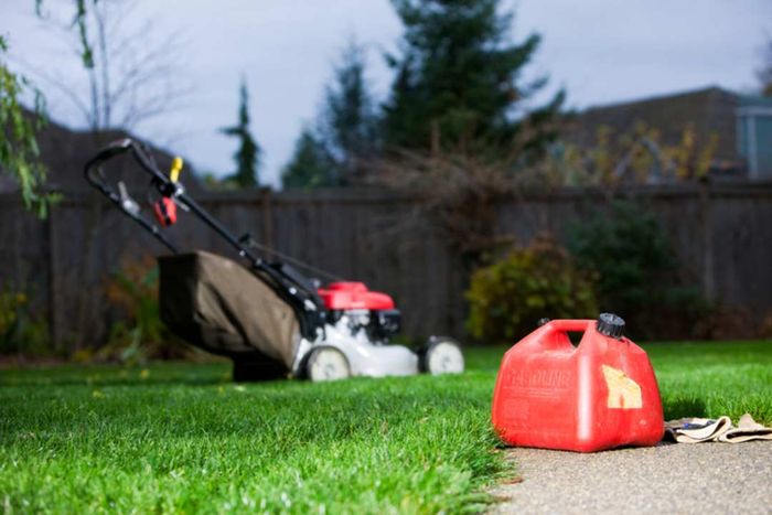 A jerrycan placed in a yard with a lawnmower visible in the background.