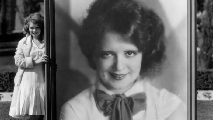 In 1928, Clara Bow stands beside a massive portrait of herself, captured by photographer Eugene Robert Richee.