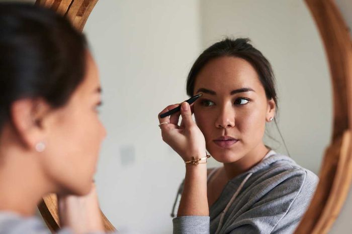 A woman styling her eyebrows in front of a mirror.