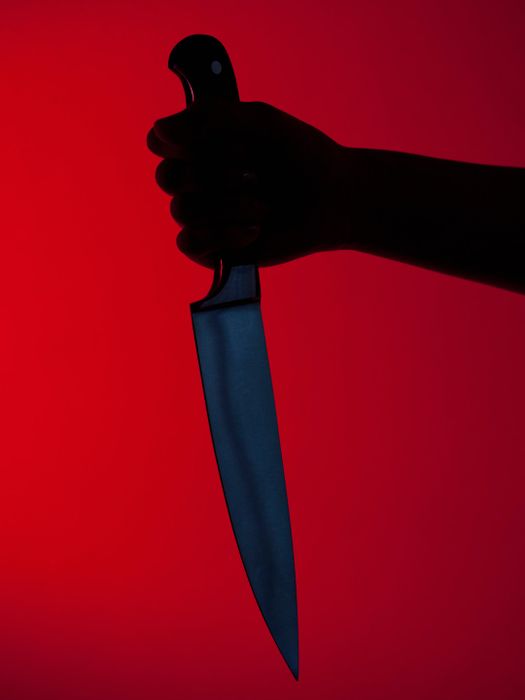 A hand gripping a blood-stained knife against a crimson backdrop