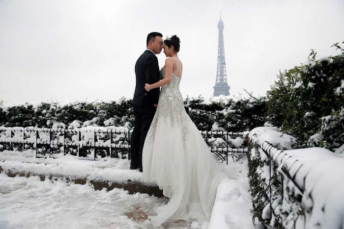 A photo of a bride and groom standing in the snow, with the Eiffel Tower visible in the background