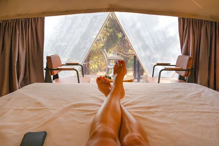 A cropped image of a woman relaxing on a bed inside a glamping dome tent.