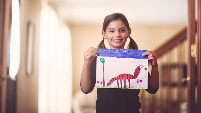 A girl holding up a drawing and smiling