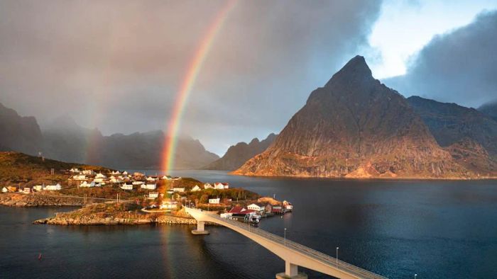 A rainbow arches over the Reine Bridge and the Olstind mountain peak in the Lofoten Islands, Norway.