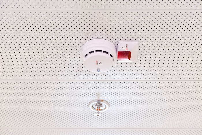 A smoke detector and sprinkler mounted in a suspended ceiling.