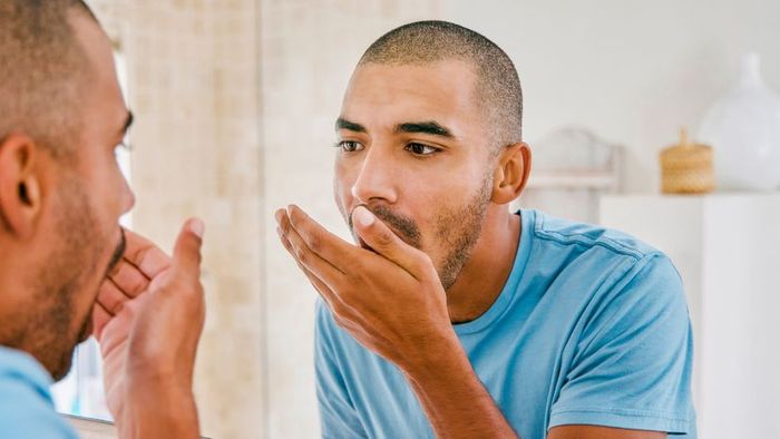 A man testing his breath in a private restroom.