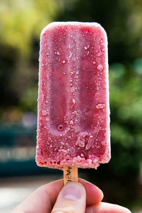 A photo of someone holding a pink, fruity popsicle outdoors