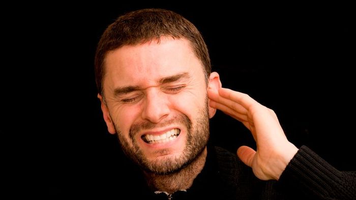 A man experiencing discomfort, holding his ear in distress