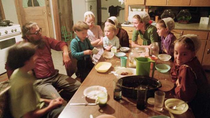An Amish family sits together for a meal at their kitchen table.