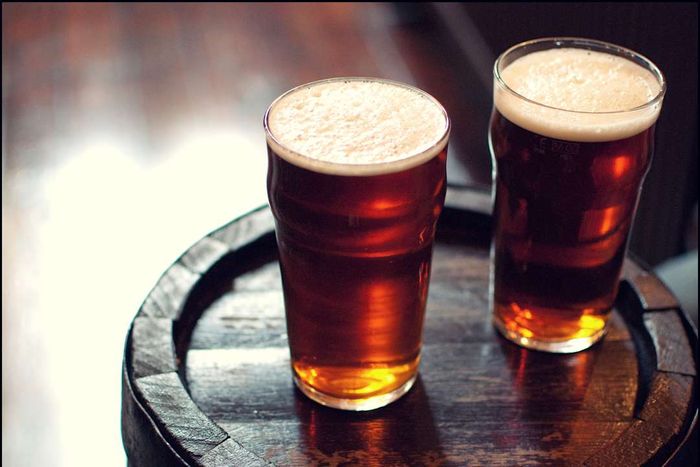 Two pints of beer resting on a barrel