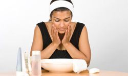 A young woman from India is washing her face, with creams and toner placed next to her wash bowl.