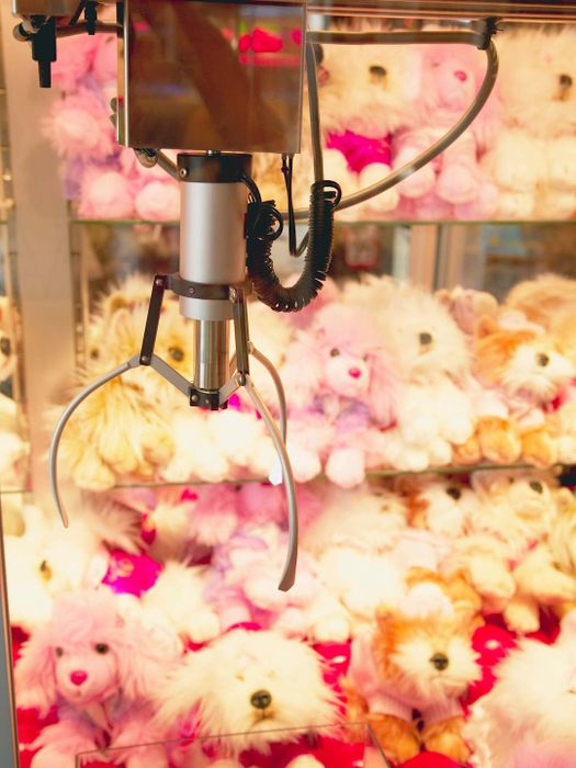 A claw poised in front of a pile of stuffed animals inside a machine