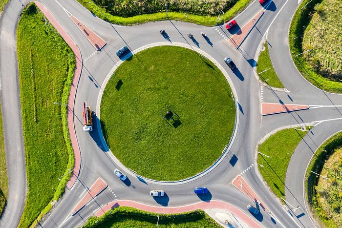 A bird’s-eye view of cars, trucks, and roadside assistance vehicles navigating a traffic circle.