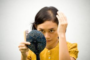 A woman examines a bald patch while looking into a mirror