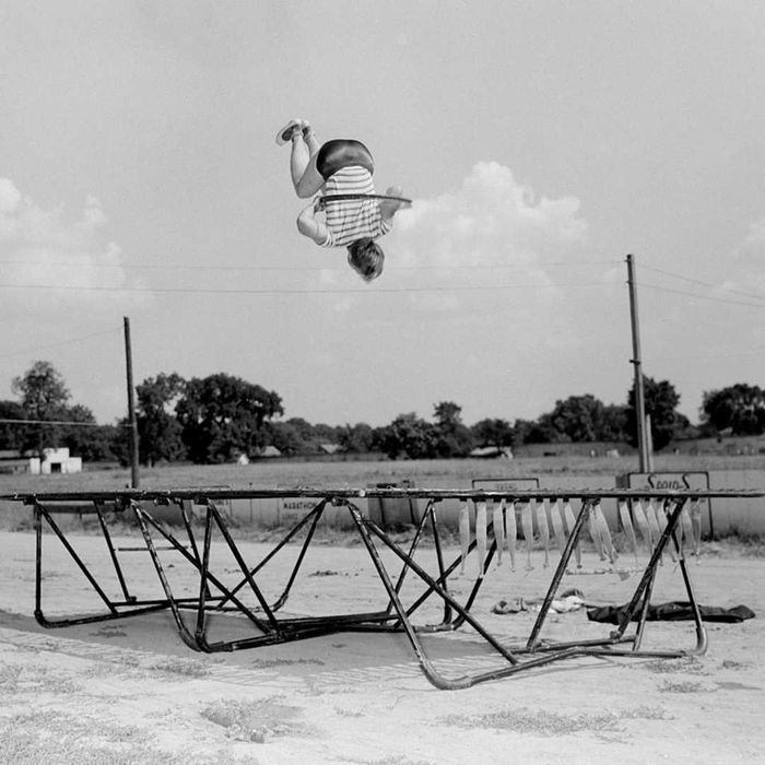 A boy wearing a hula hoop jumps on a trampoline, circa 1955