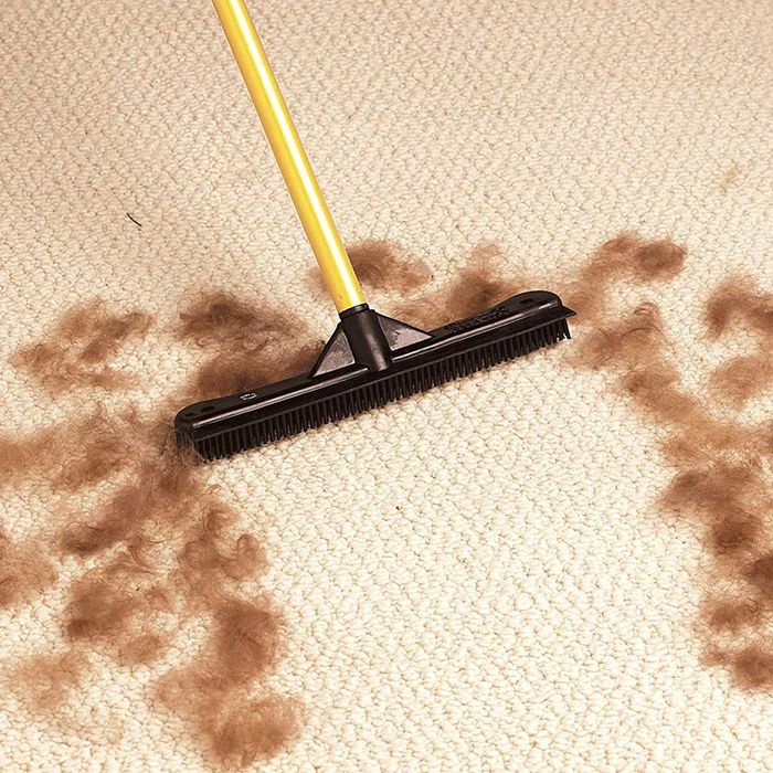 A FURemover Pet Hair Remover Carpet Rake in action on a carpet surrounded by pet hair.