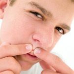 A teenage boy squeezing a pimple on his face.