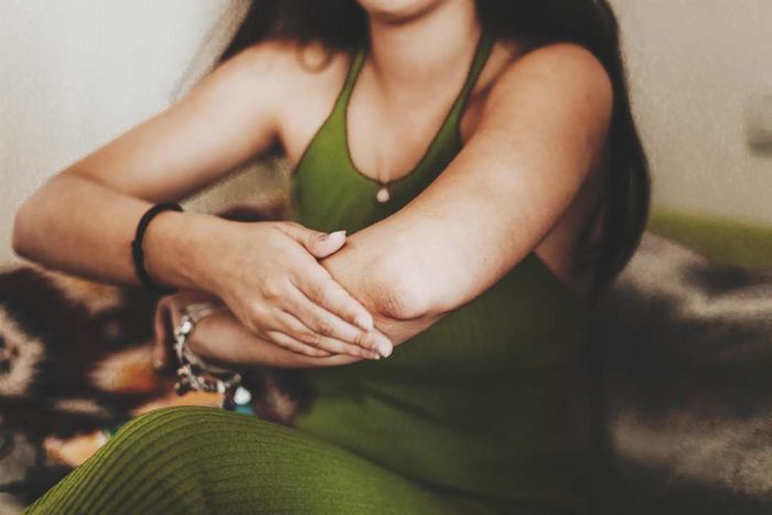 A woman gently rubs moisturizer onto her elbow.