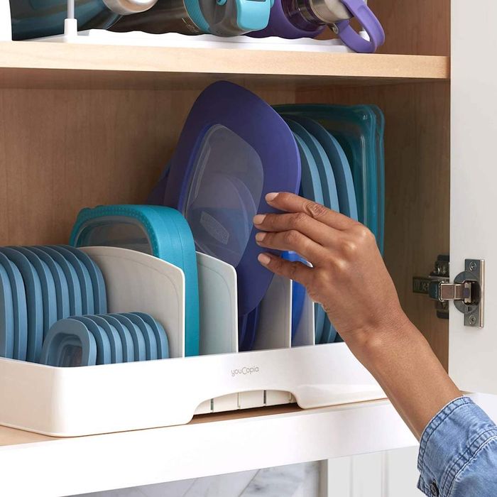 A close-up of the YouCopia StoraLid Organizer with blue lids inside, featuring a hand holding one of the lids.