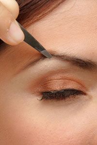 A woman shaping her eyebrows with tweezers.