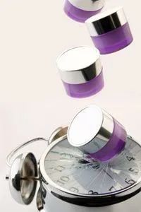 Jars of moisturizing creams topple onto an alarm clock, freezing time in its tracks