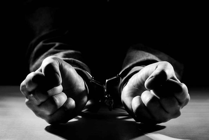 A monochrome image depicting hands restrained by handcuffs
