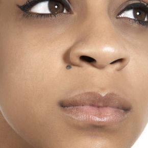 A close-up portrait of a young woman featuring a distinctive facial mole.