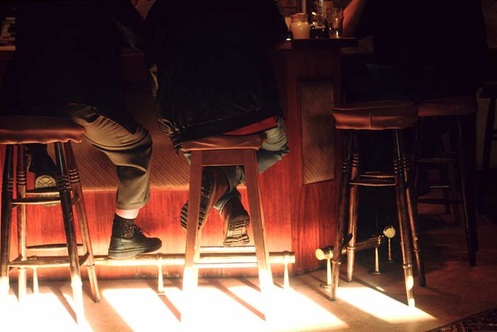 Men seated on stools in a pub with sunlight streaming across the floor