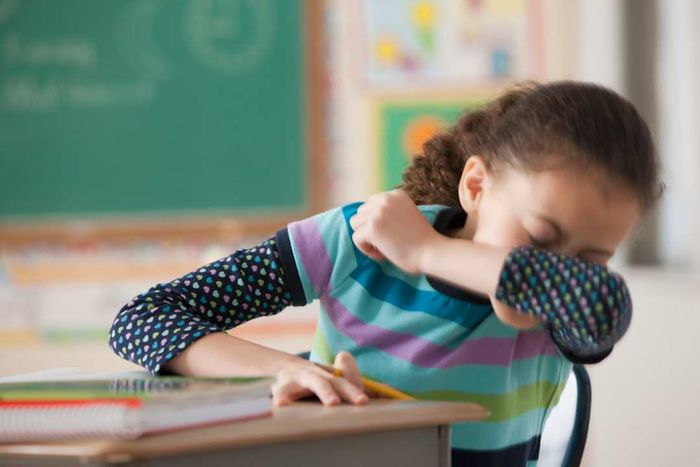 A child sneezing into her elbow