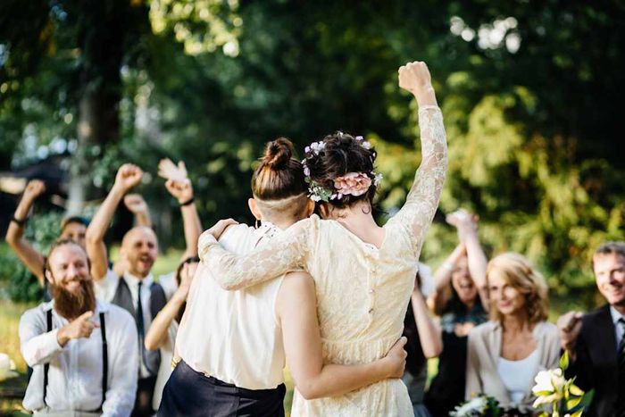 Two women newly married, walking down the aisle as loved ones celebrate