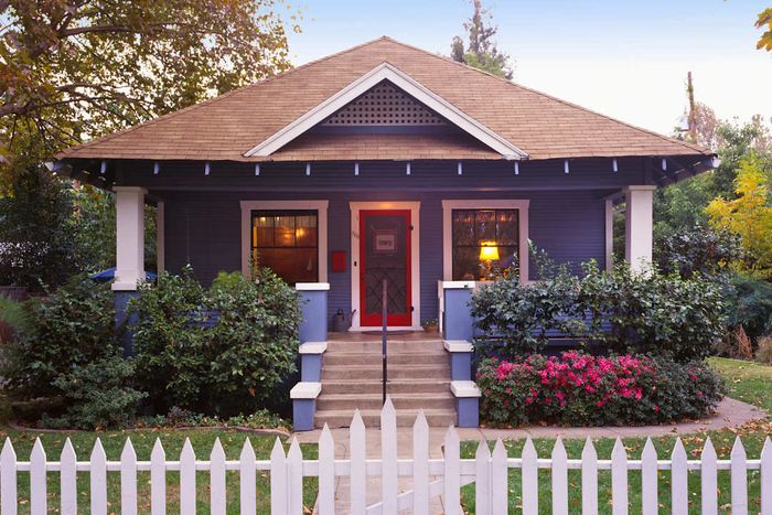 A blue Craftsman house with a white picket fence in front of it.