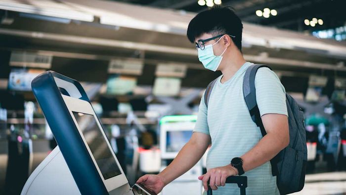A young man wearing a protective face mask while checking in at an airport.