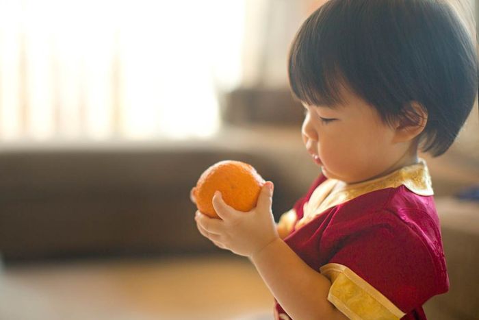 Close-up of a toddler dressed in traditional Chinese attire holding a tangerine.
