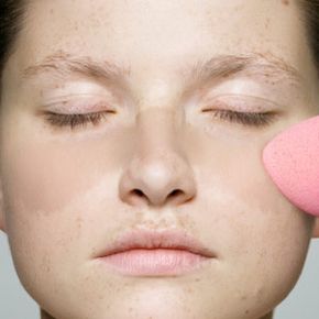 A woman with a freckled face applies foundation to conceal her freckles.