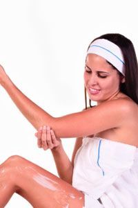 A young woman gently applying moisturizer to her elbow for hydration and softness.