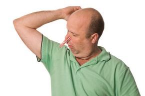 A man experiencing sweaty underarms, holding a clothes peg to his nose.